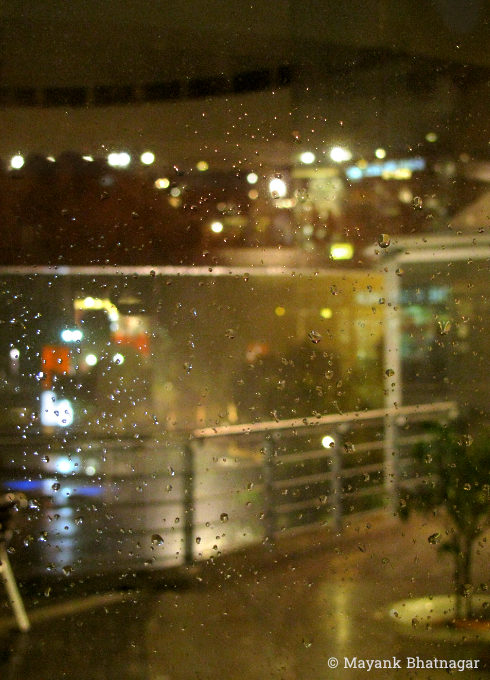Water droplets on glass in the foreground and blurred railing of the mall and buildings in the background