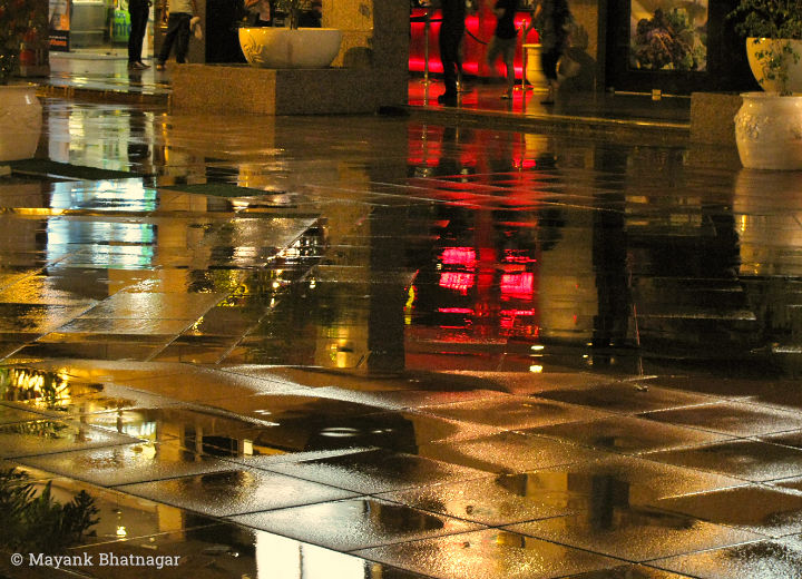 Reflections of colorful lights and building exterior on wet floor tiles