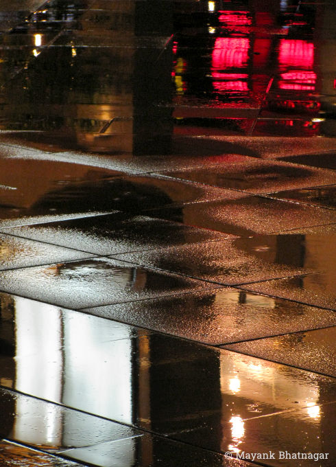Reflections of red, yellow and white lights on wet floor tiles, at night