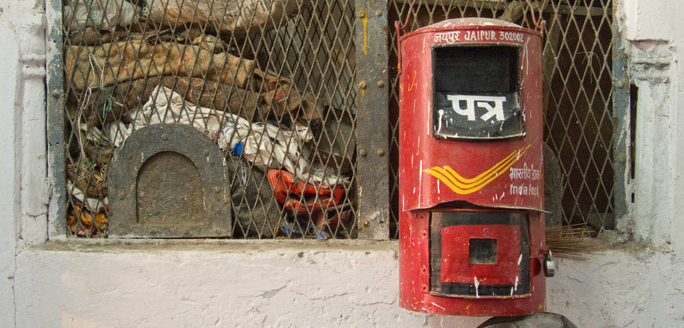 A red postbox / letterbox hanging from an old, defunct iron and iron mesh post office counter