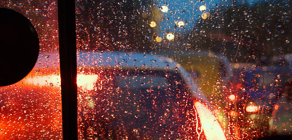 Painterly photograph of cars waiting at a traffic stop at night, taken through a raindrop splattered windscreen