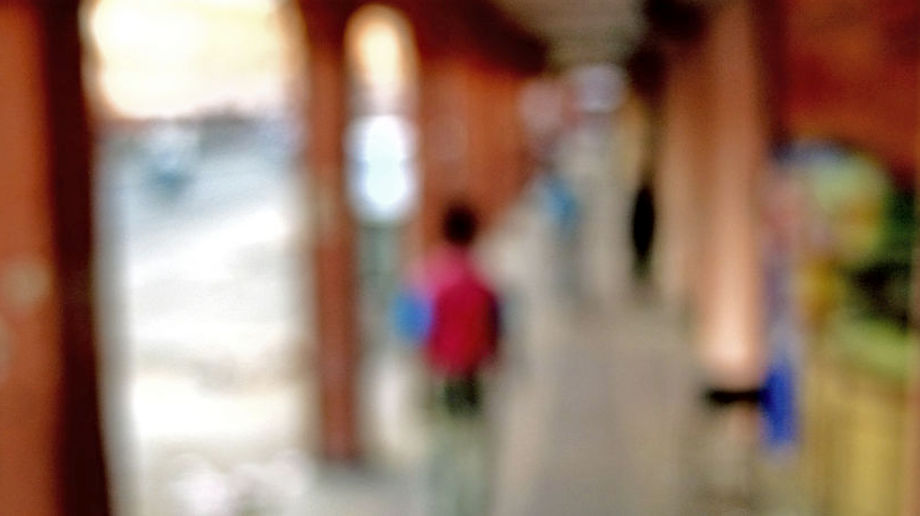 Blurred image of people walking in a corridor with shops to their right and a street to their left